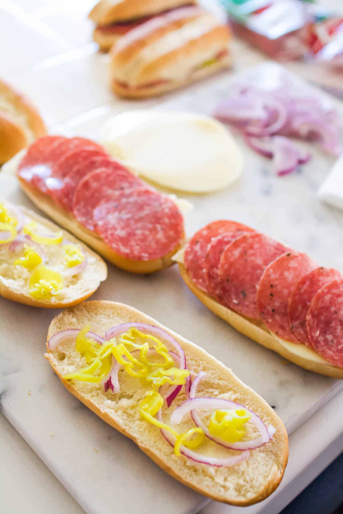 A few hot salami sandwiches being made on a cutting board.