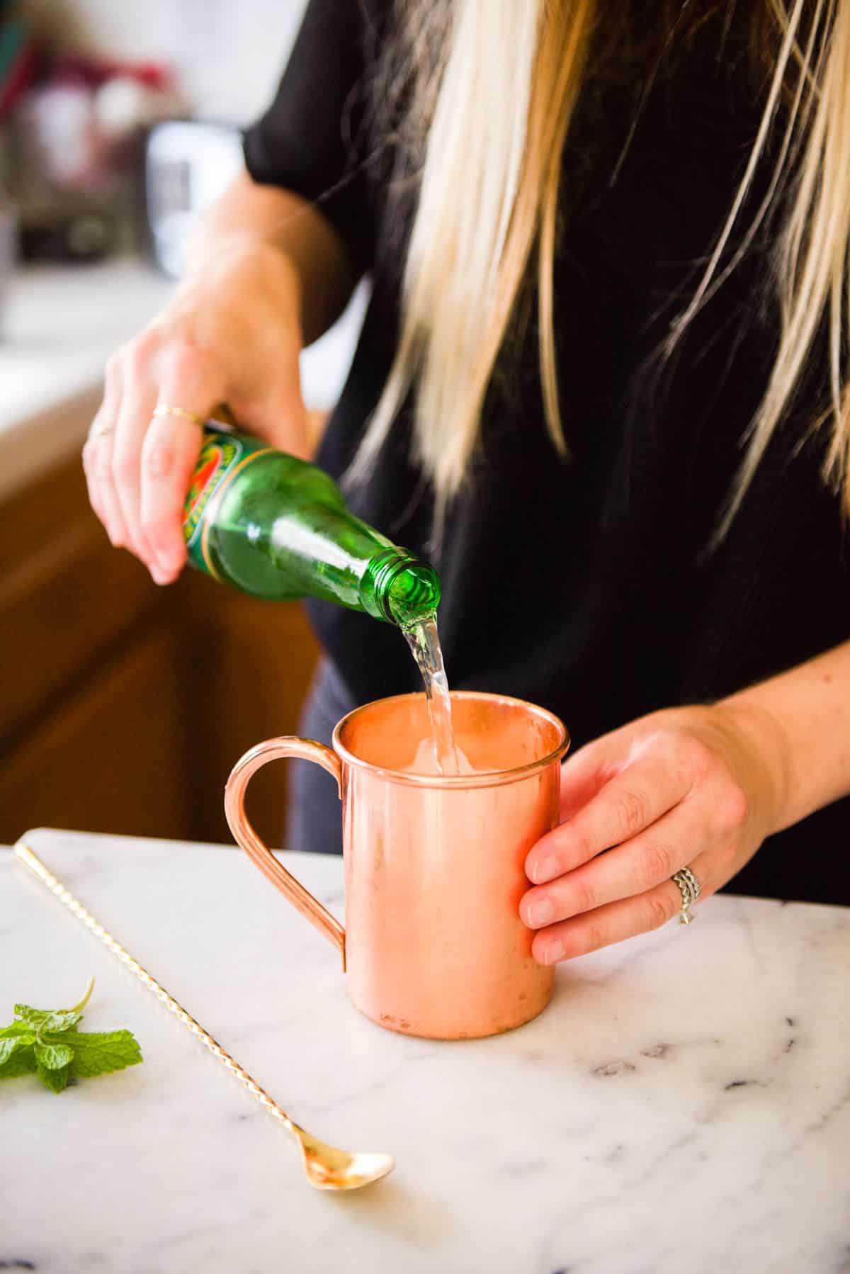 Woman pouring ginger beer into a copper mug.