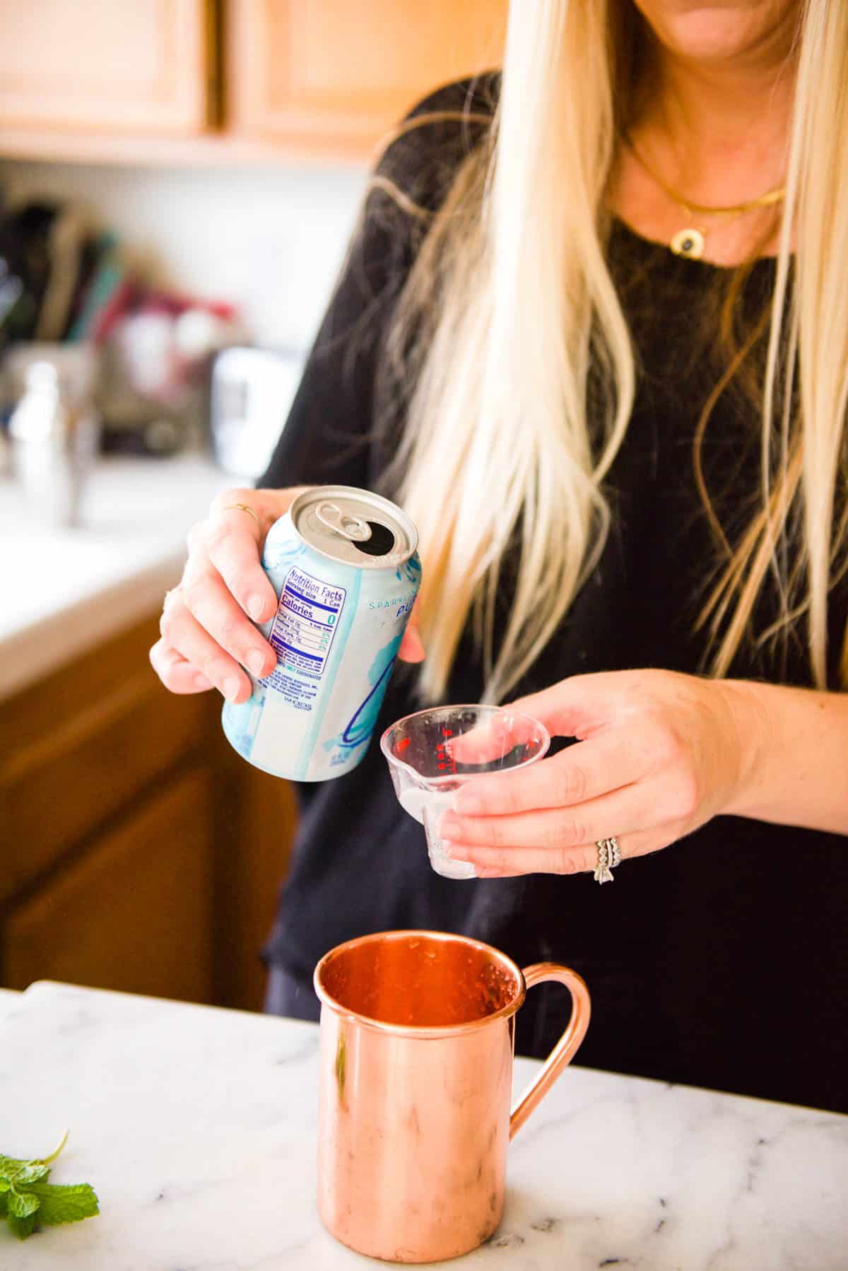 Woman measuring club soda in a jigger.