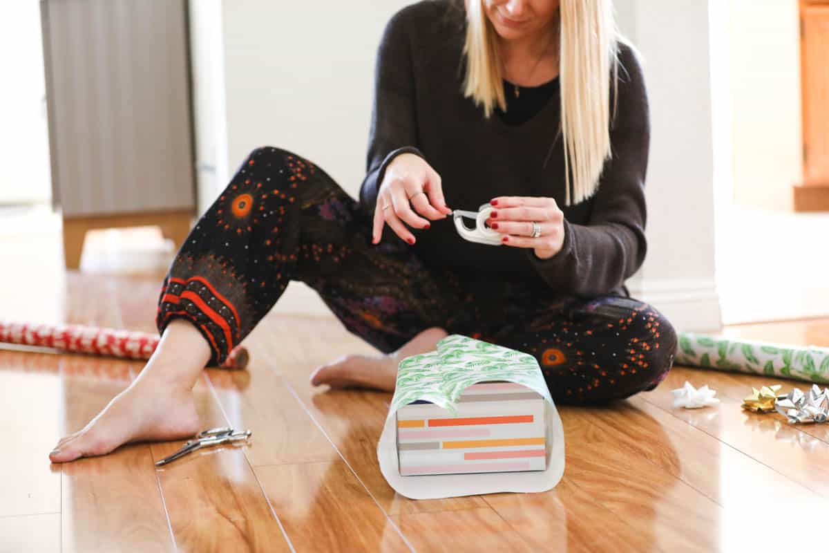 Woman sitting on the floor and pulling off tape for wrapping a present.