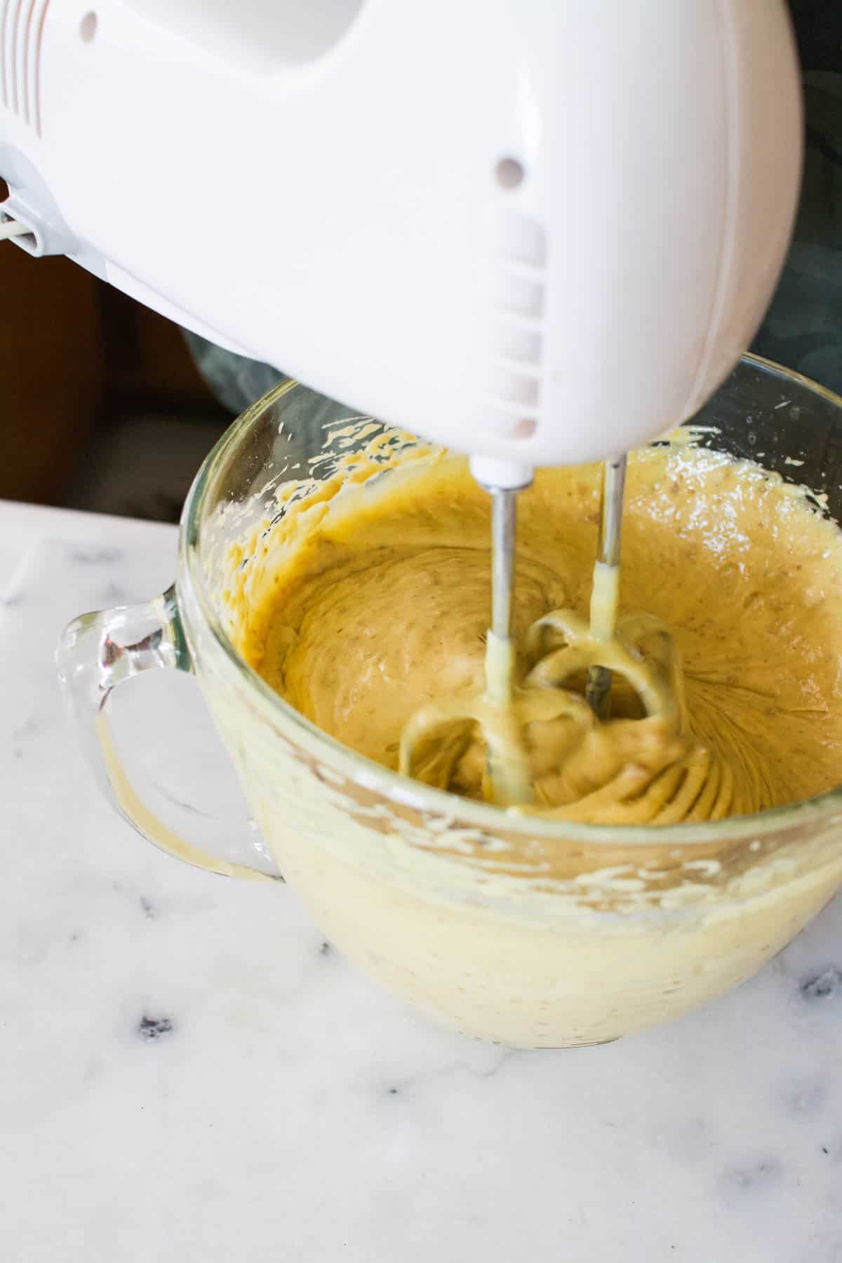 Woman using a hand mixer to mix cake batter.