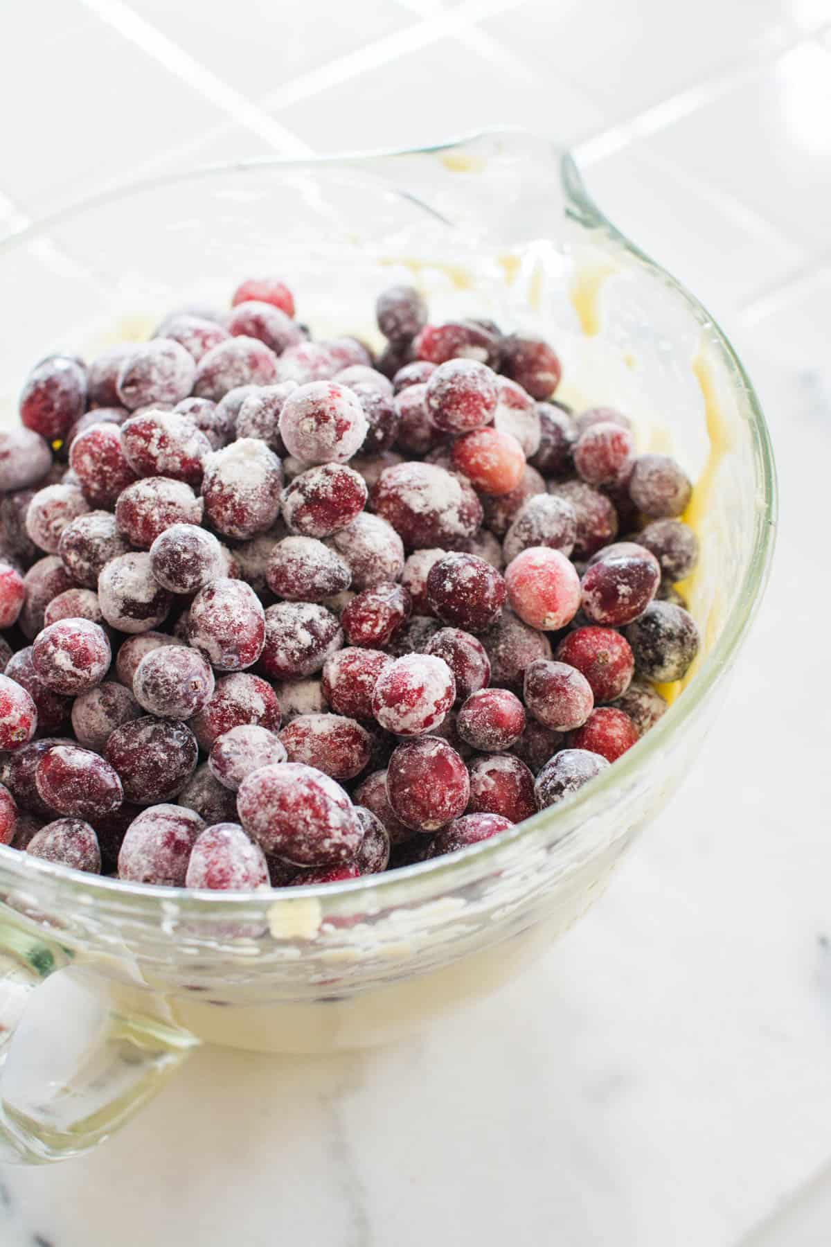 Floured cranberries on top of cake batter in a glass mixing bowl.