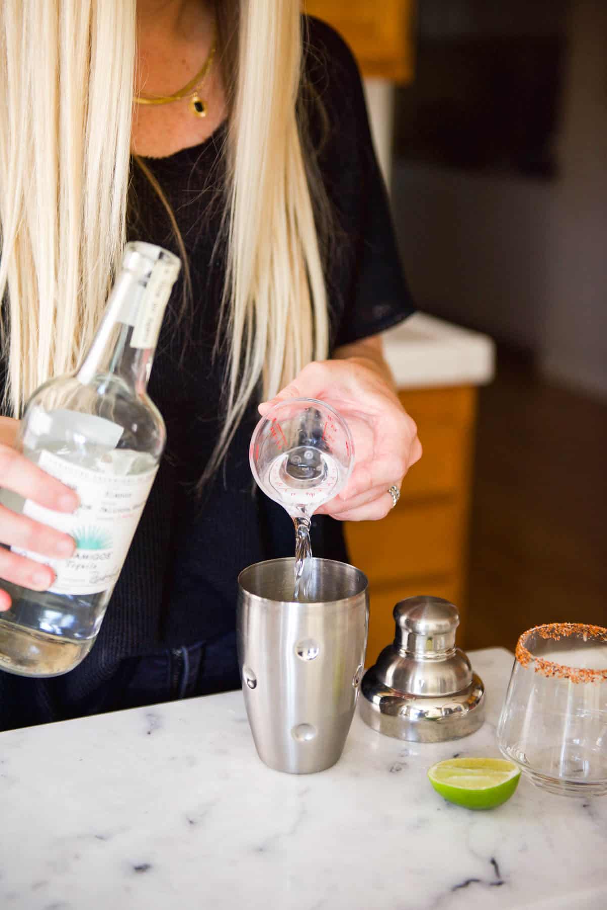 Woman adding tequila to a cocktail shaker.