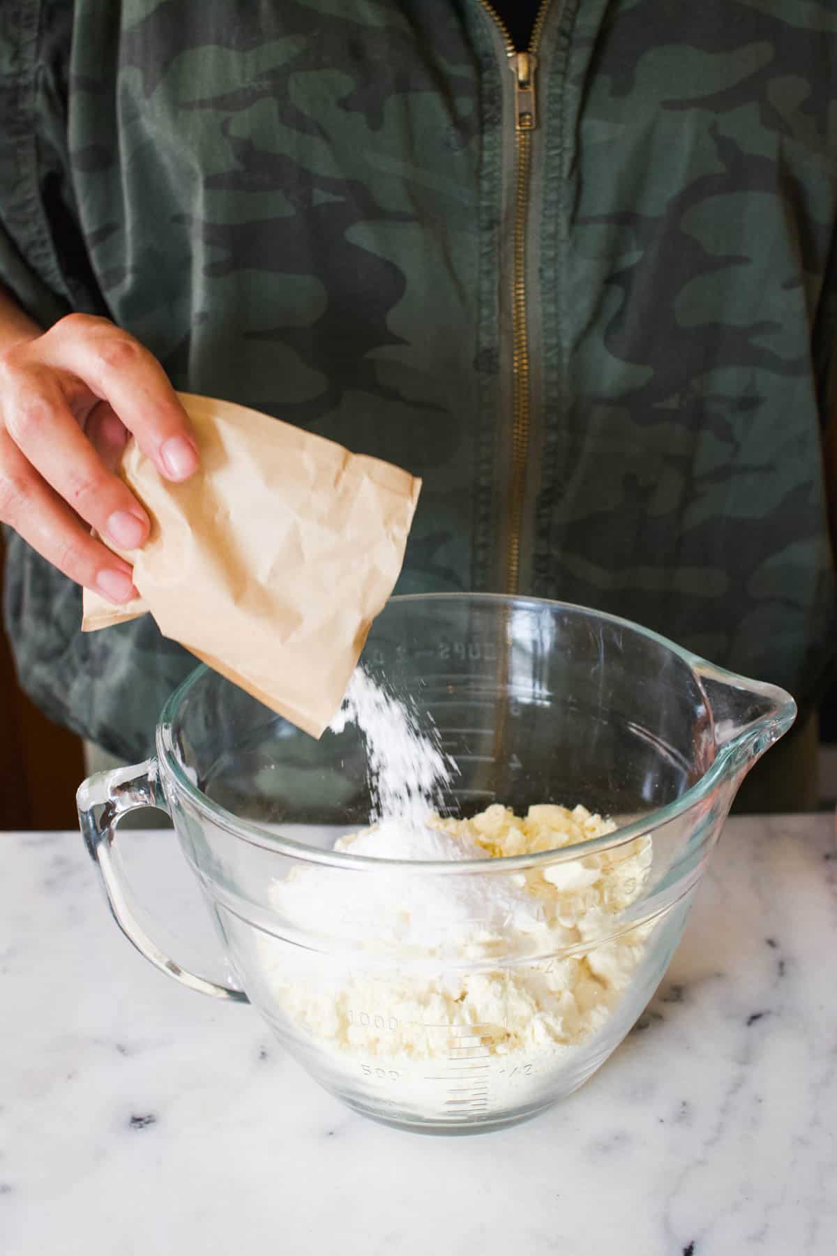 Woman adding dry pudding powder to a batter bowl with cake mix.