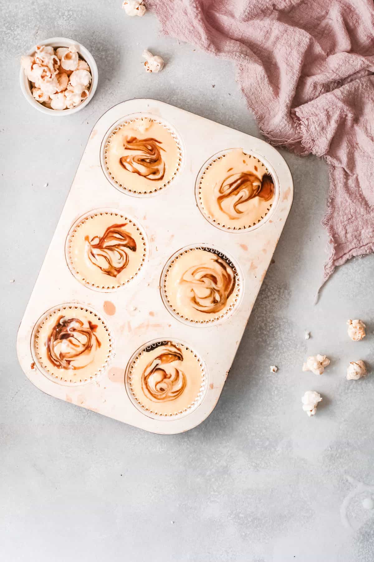 Cupcake tin with batter topped with caramel sauce.