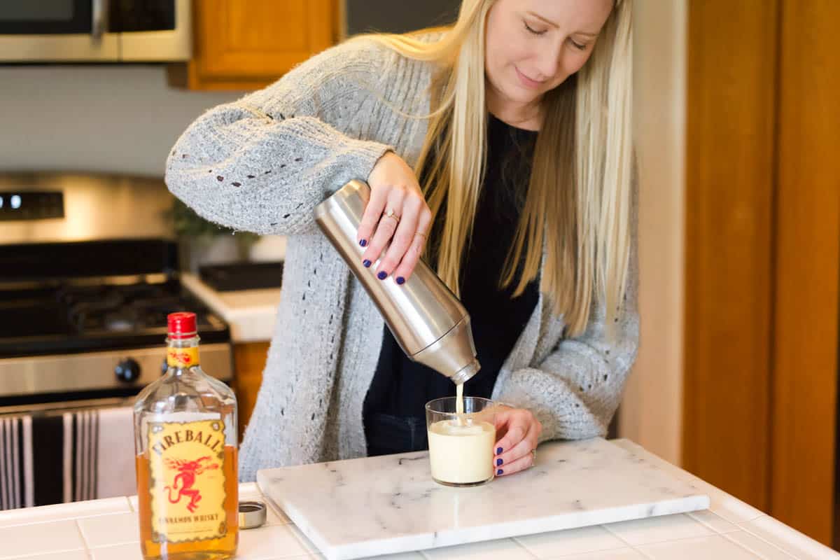 Woman pouring a cocktail from a cocktail shaker into a glass on the counter.