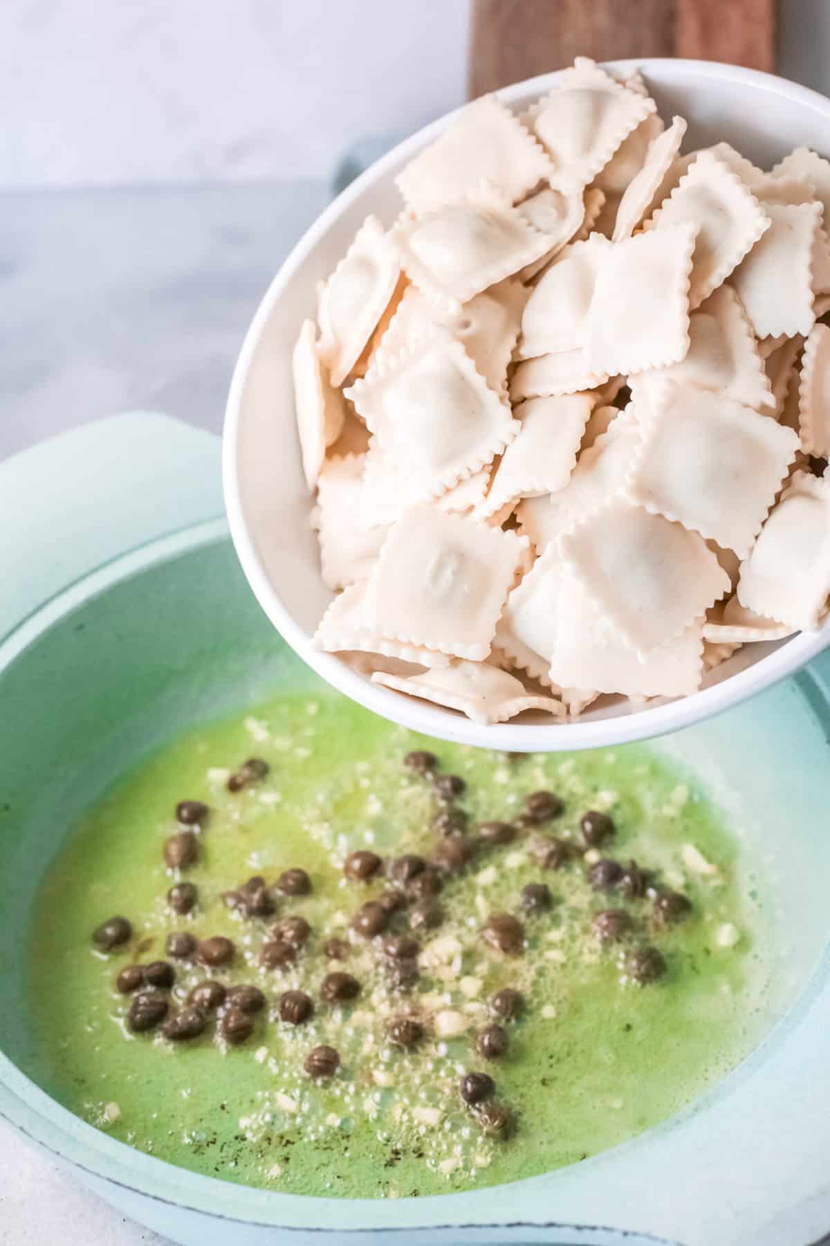 Woman adding ravioli to a bowl with melted butter, capers and garlic.