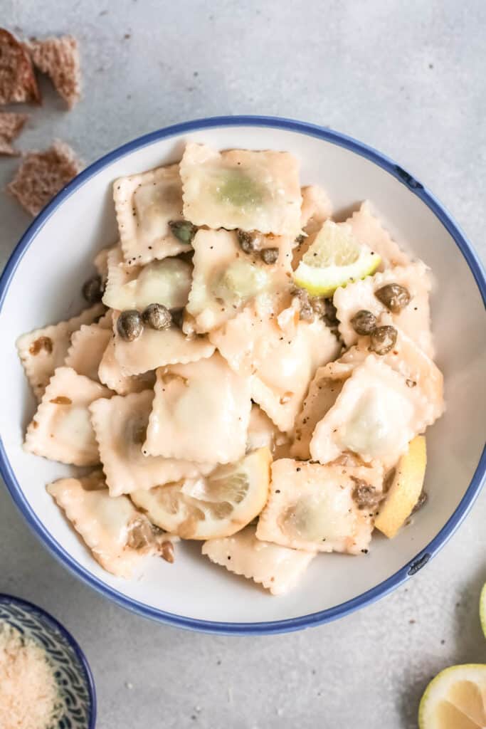 Overhead shot of a bowl of raviolis with pieces of lemon and capers.