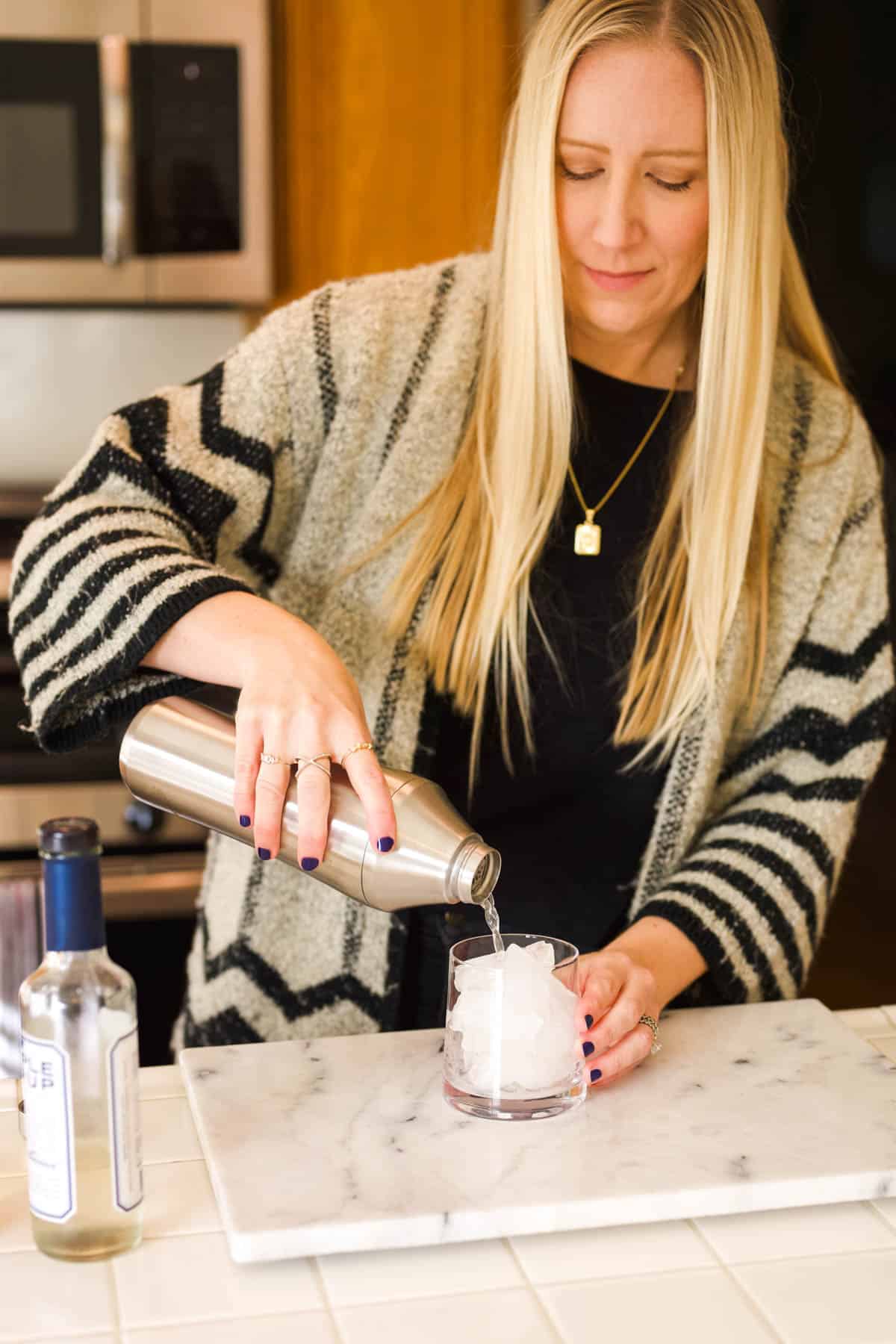 Woman pouring an Amaretto Sour out of a cocktail shaker into a cocktail glass.