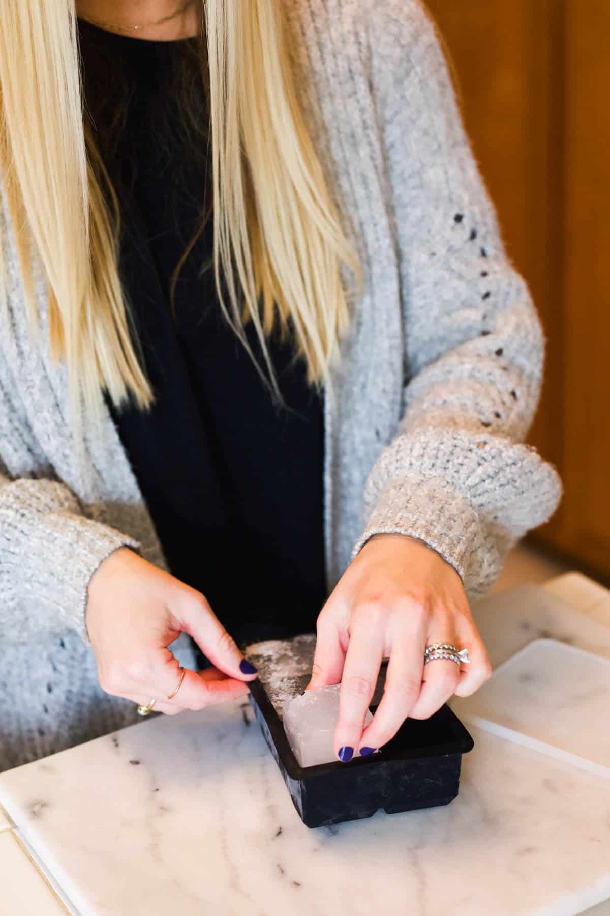 Woman taking a large square ice cube out of a tray.