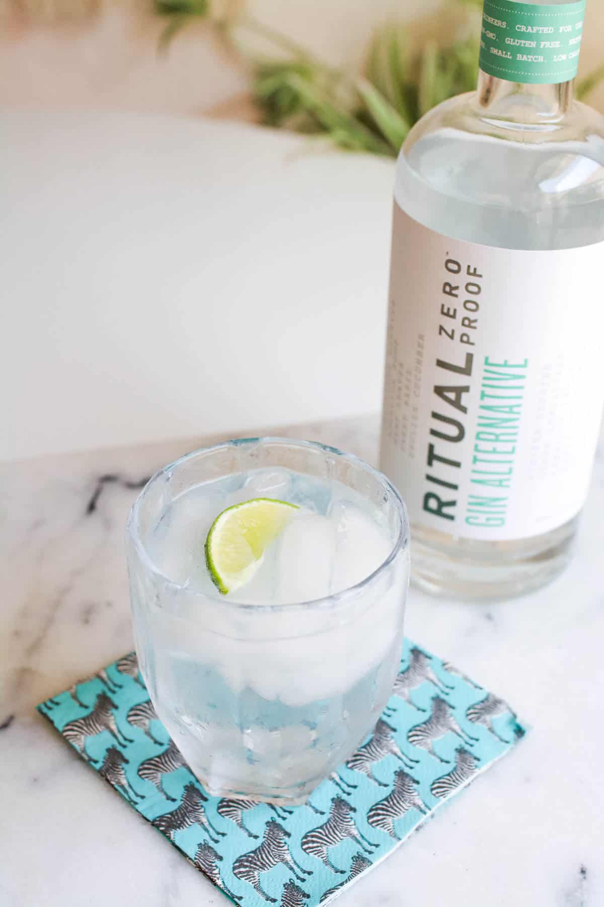 Short cocktail glass on a table with a wedge of lime next to a bottle of Ritual Zero Proof Gin.