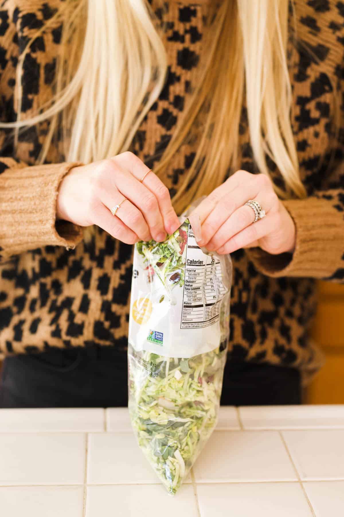 Woman opening a bag of salad mix.