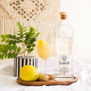 A yellow cocktail next to a bottle of Lobos tequila on a table.