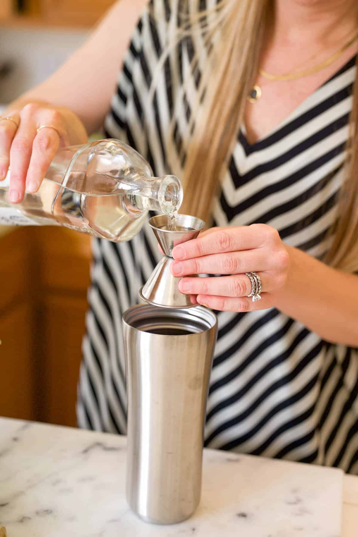 Woman measuring tequila in a jigger over a cocktail shaker.