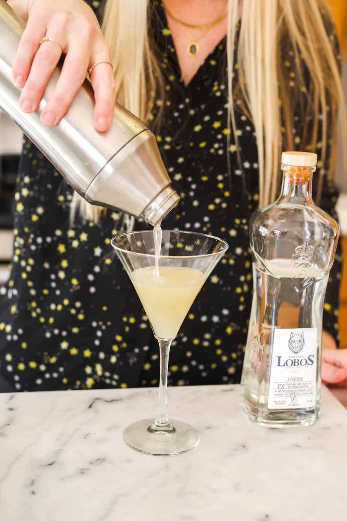 Woman straining a cocktail into a martini glass.