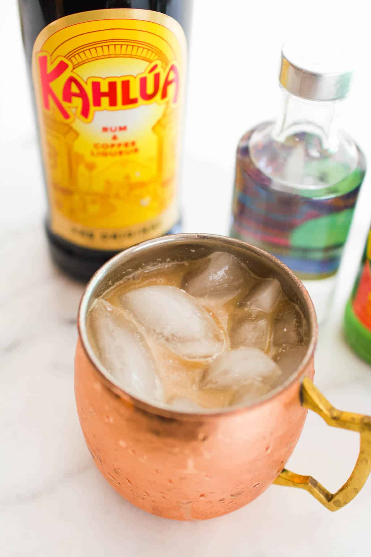 An overhead shot of the contents of a White Russian Mule in a copper mug next to vodka and Kahlua.