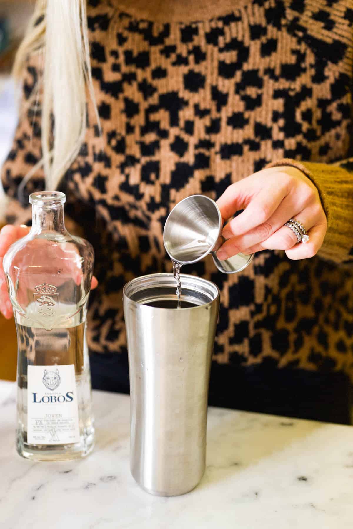 Woman adding tequila to a cocktail shaker.