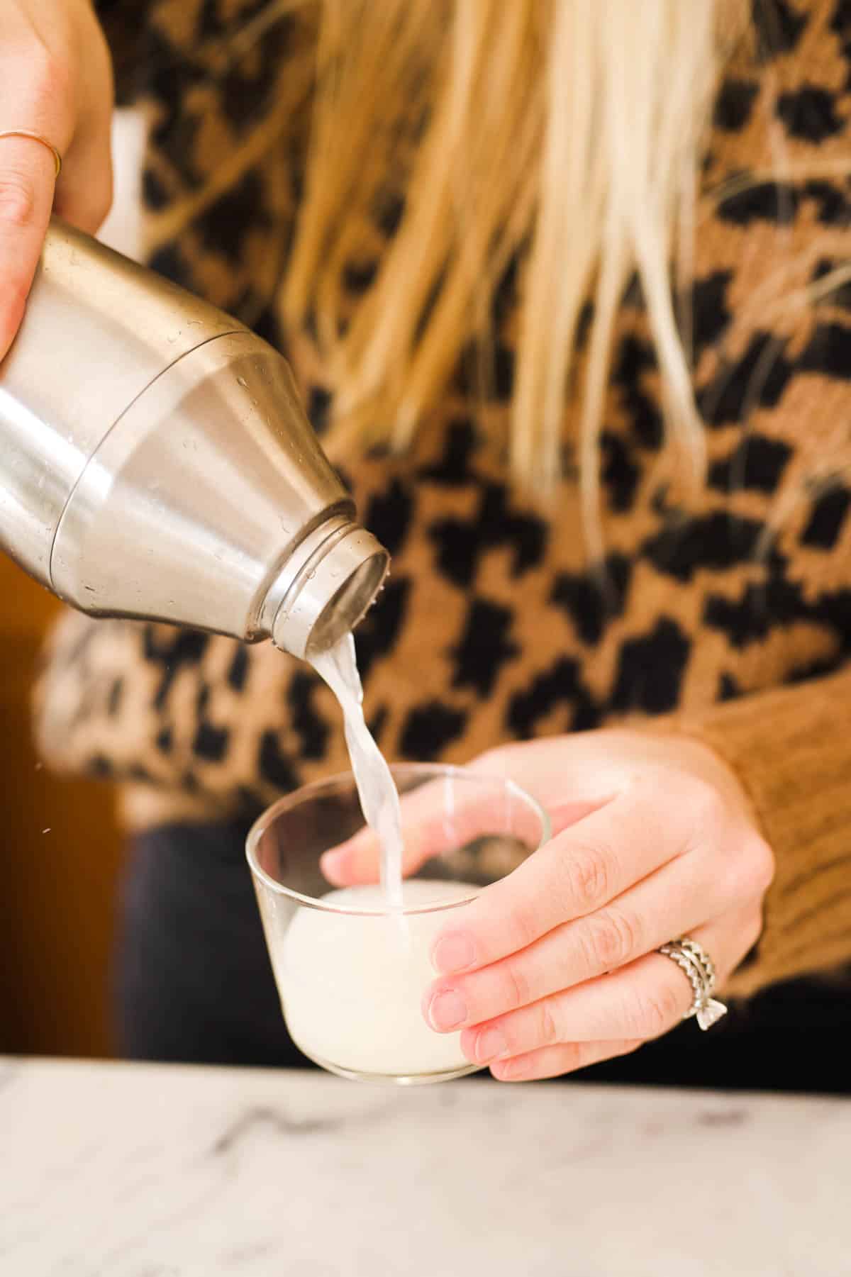 Woman straining a tequila sour from a cocktail shaker into a short glass.