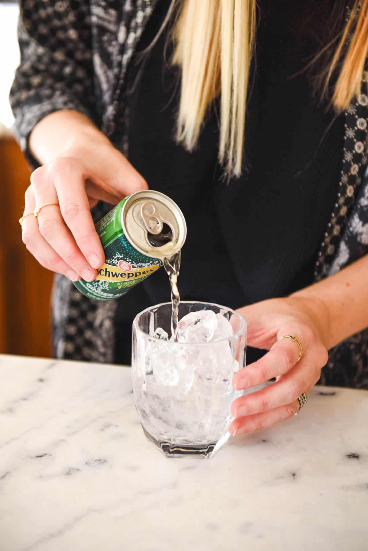 Woman pouring ginger ale into a cocktail glass.