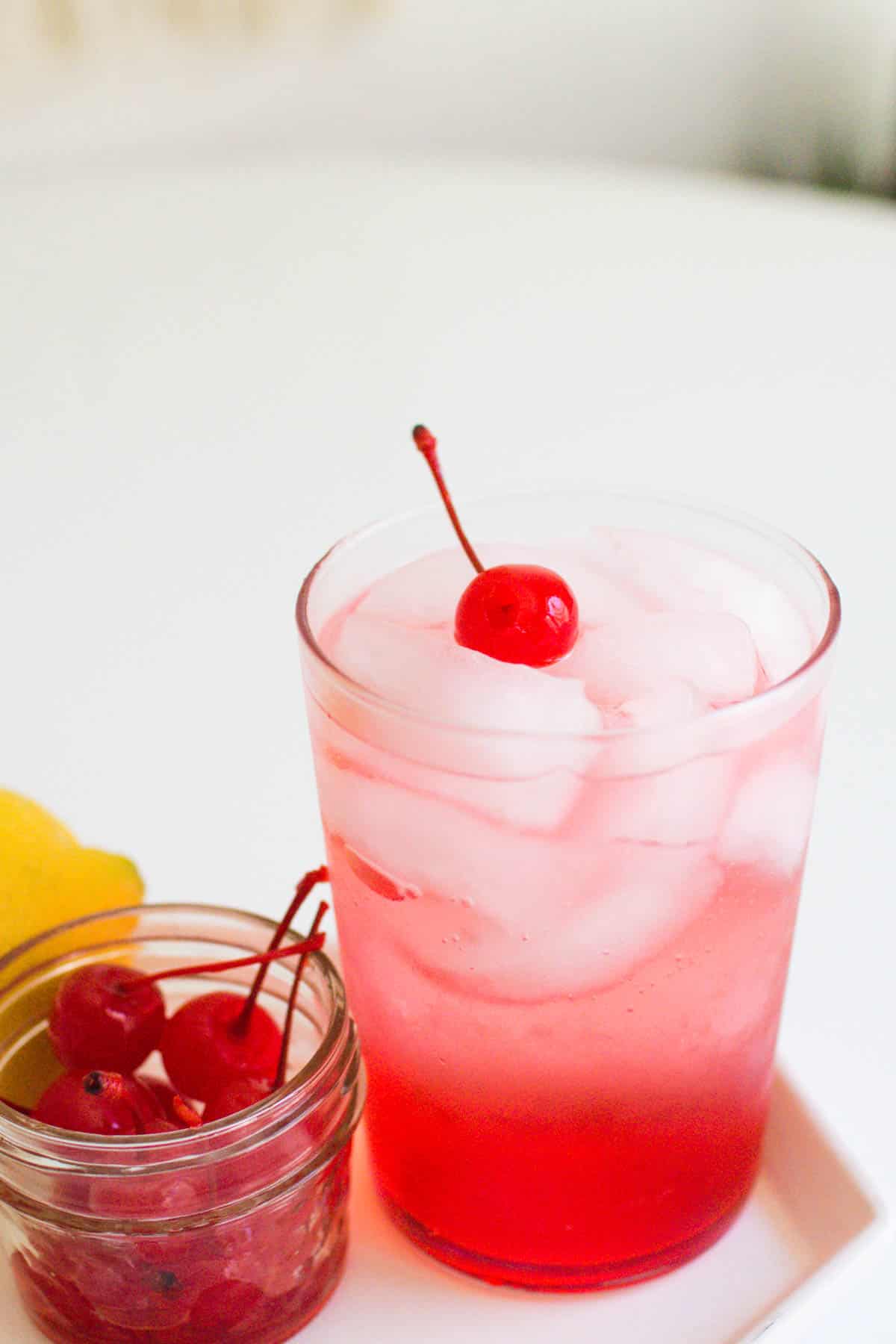 A cocktail glass holding a pink cocktail with a cherry on top.