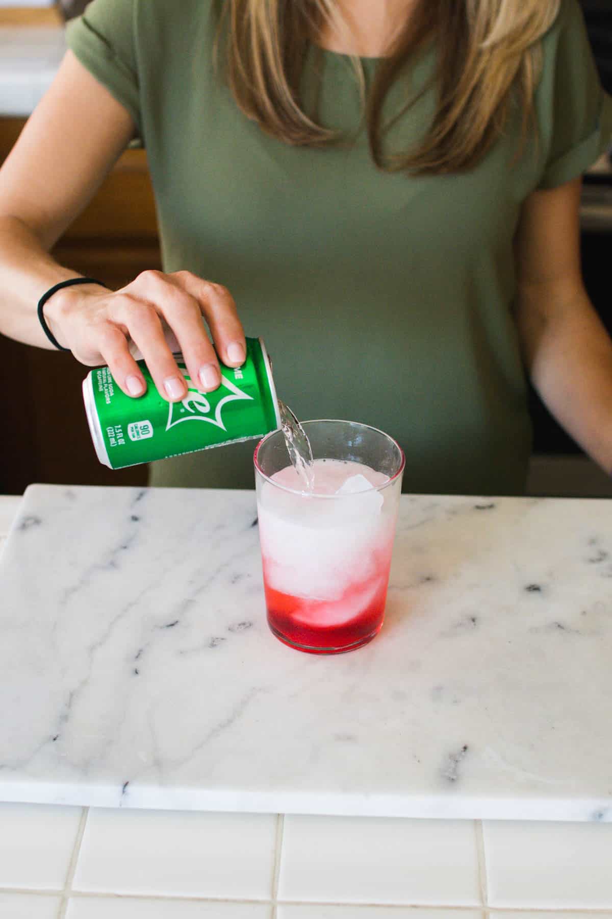 Woman adding lemon lime soda to a cocktail with grenadine in the bottom.