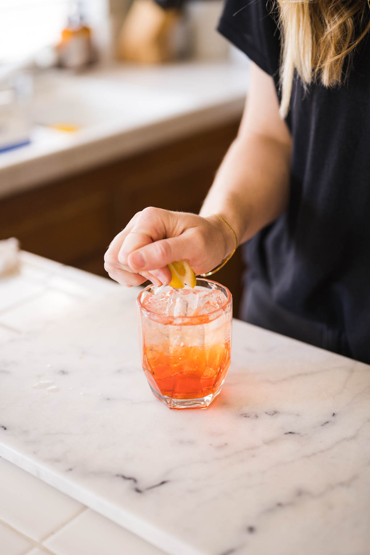 Woman squeezing lemon into a cocktail on a counter.