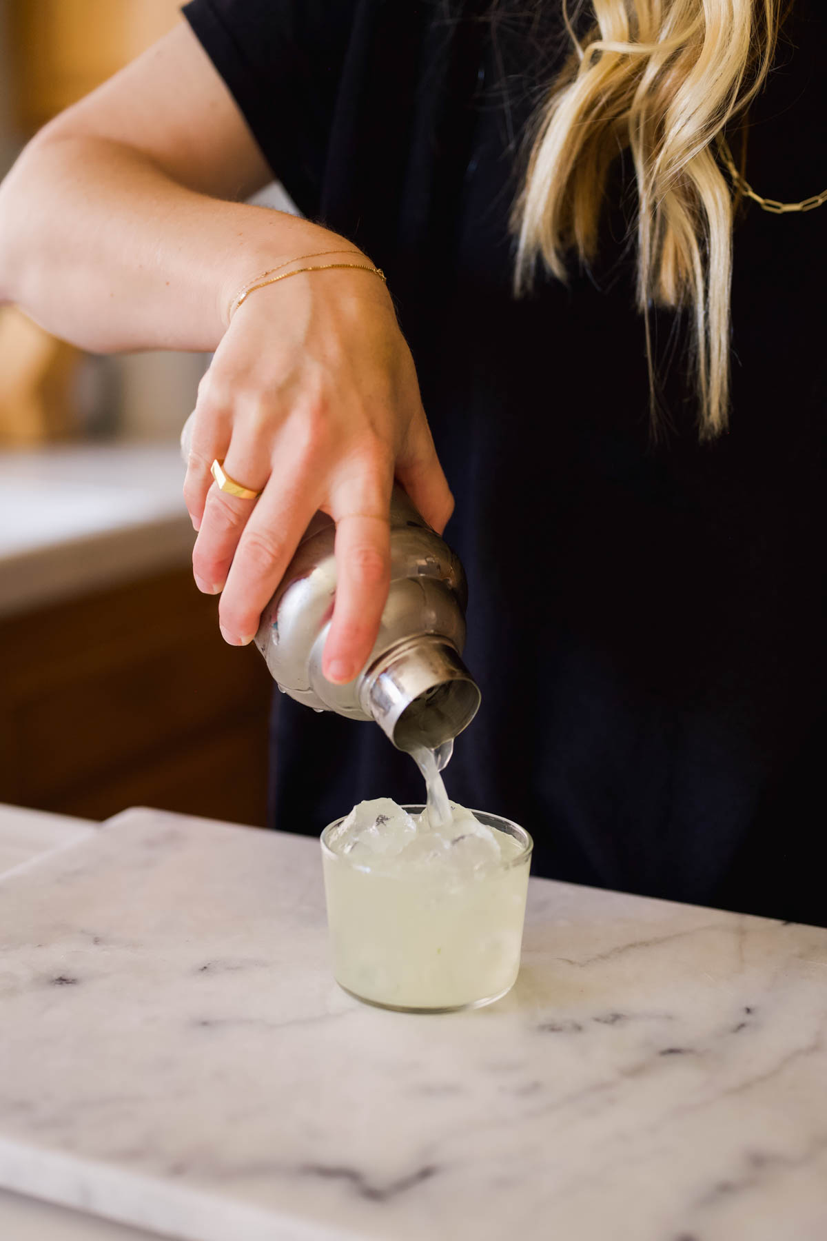 Woman straining a cocktail into a short glass.