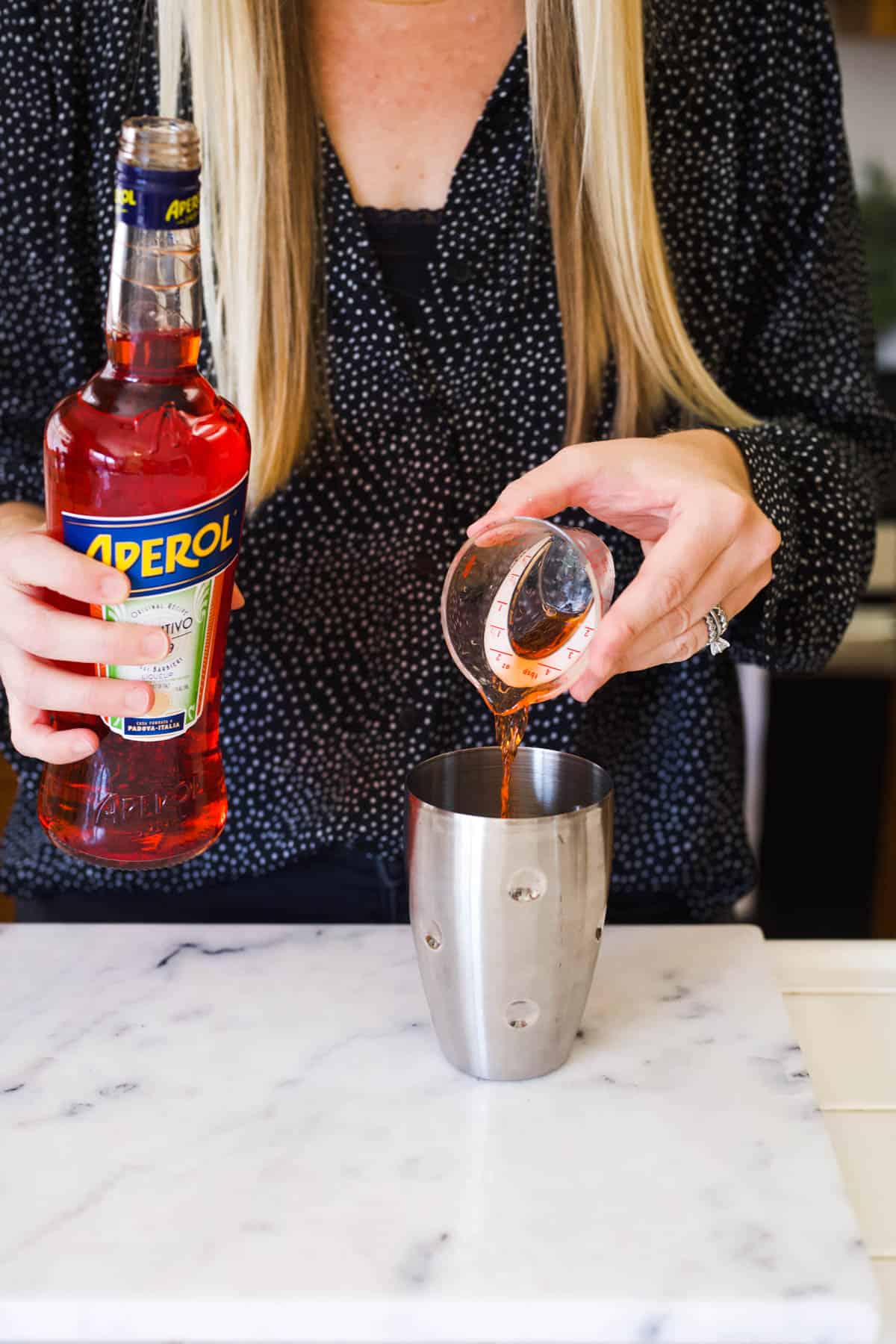 Woman adding Aperol to a cocktail shaker.