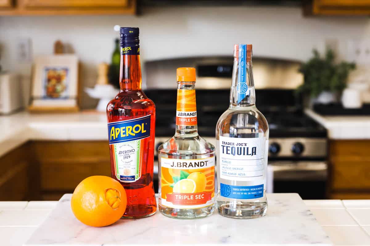 Ingredients to make a margarita with Aperol liqueur on a counter.