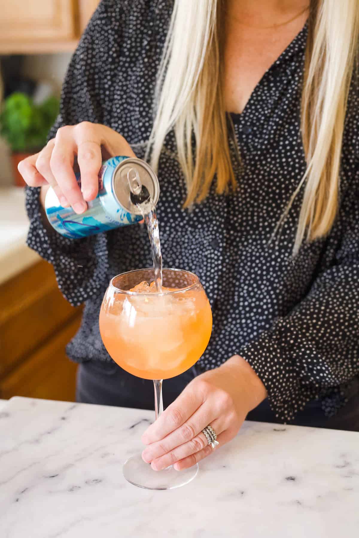 Adding club soda to a watermelon aperol spritz in a cocktail glass.