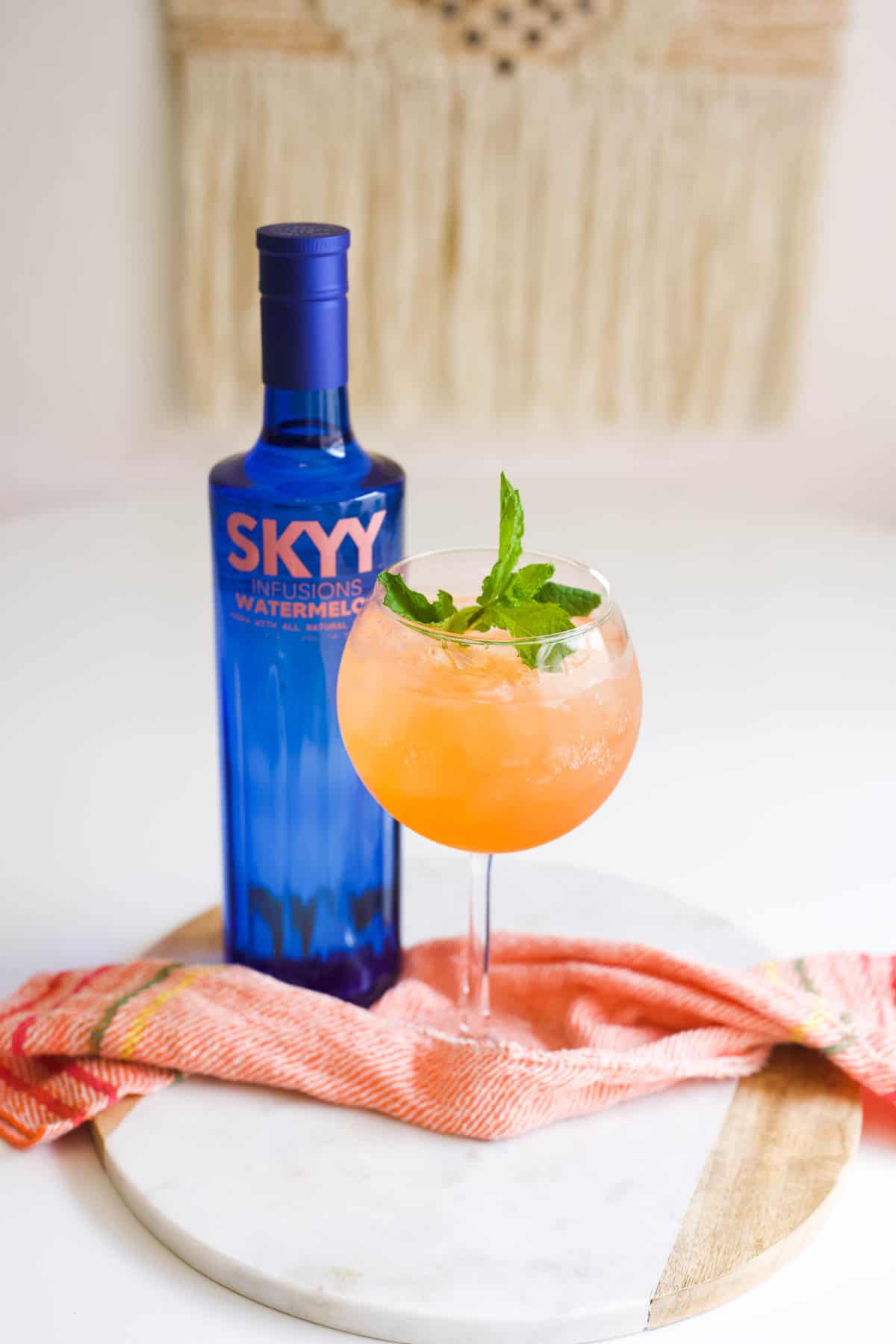 Bottle of Skyy Watermelon vodka next to a wine glass with a watermelon vodka cocktail.