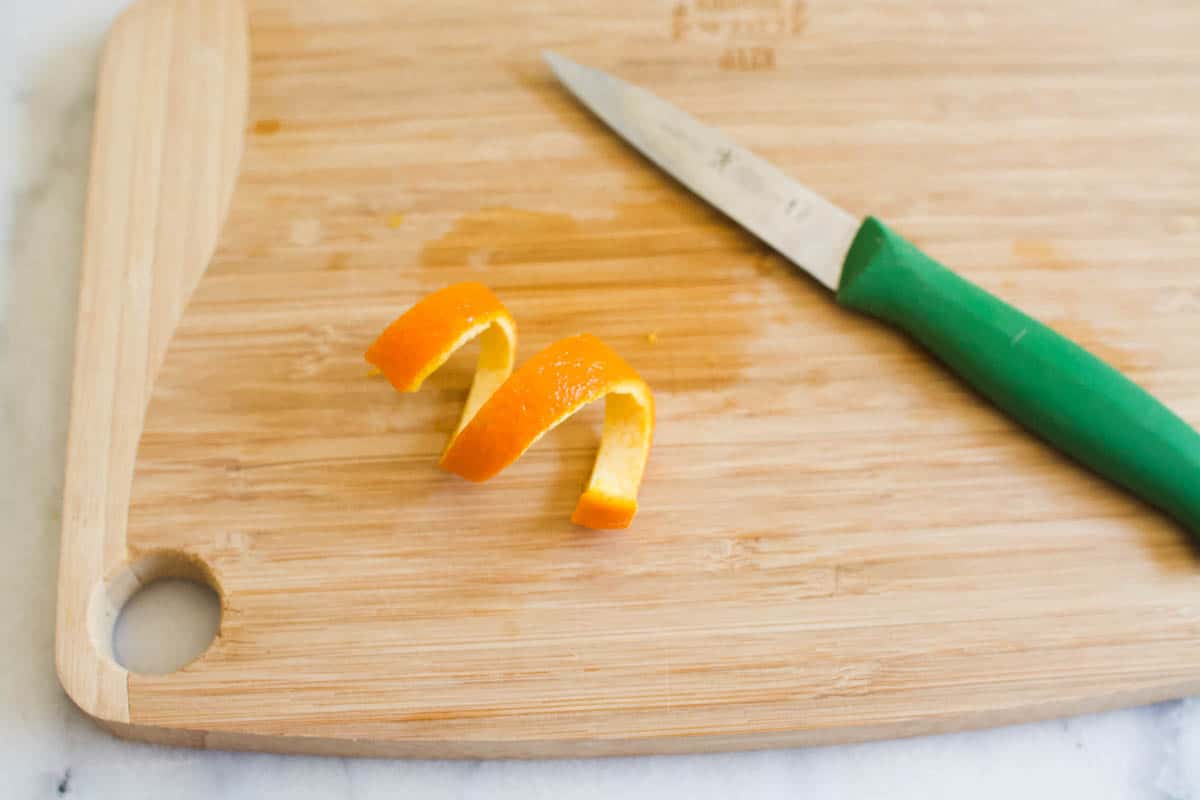 A wooden cutting board with an orange peel twist and a pairing knife.