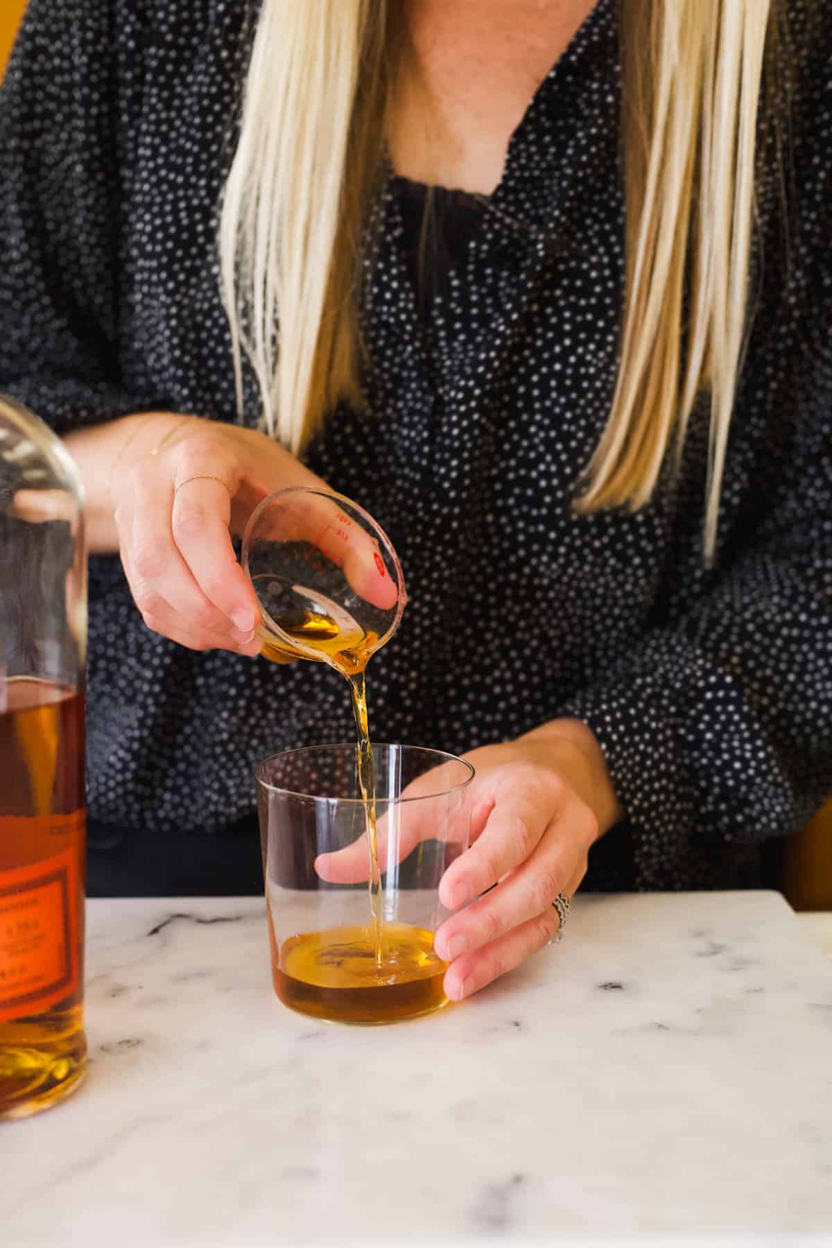 Woman adding Cinnamon Whiskey to a cocktail glass.