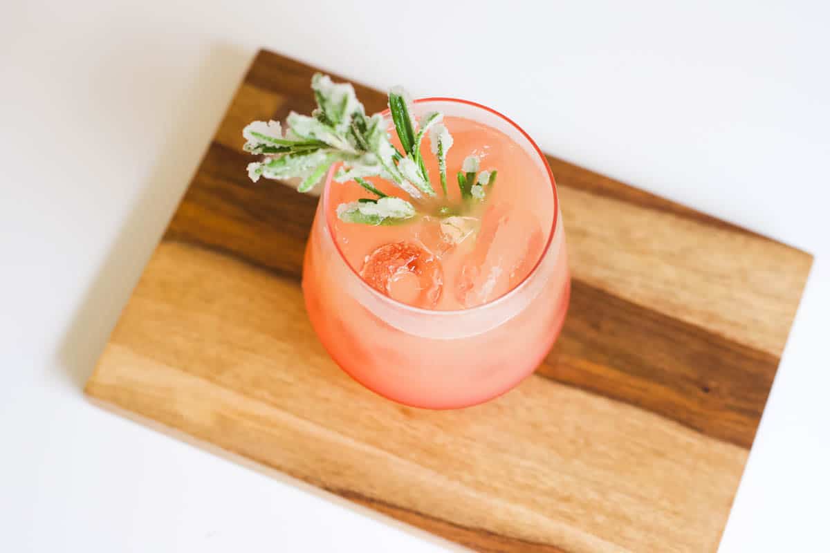 Sugared rosemary garnish in a cocktail on a wooden tray.