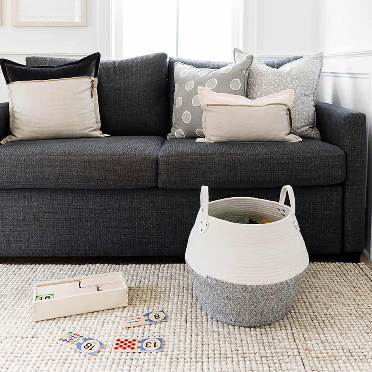 A couch with toys and a fabric basket on the floor in front of it.