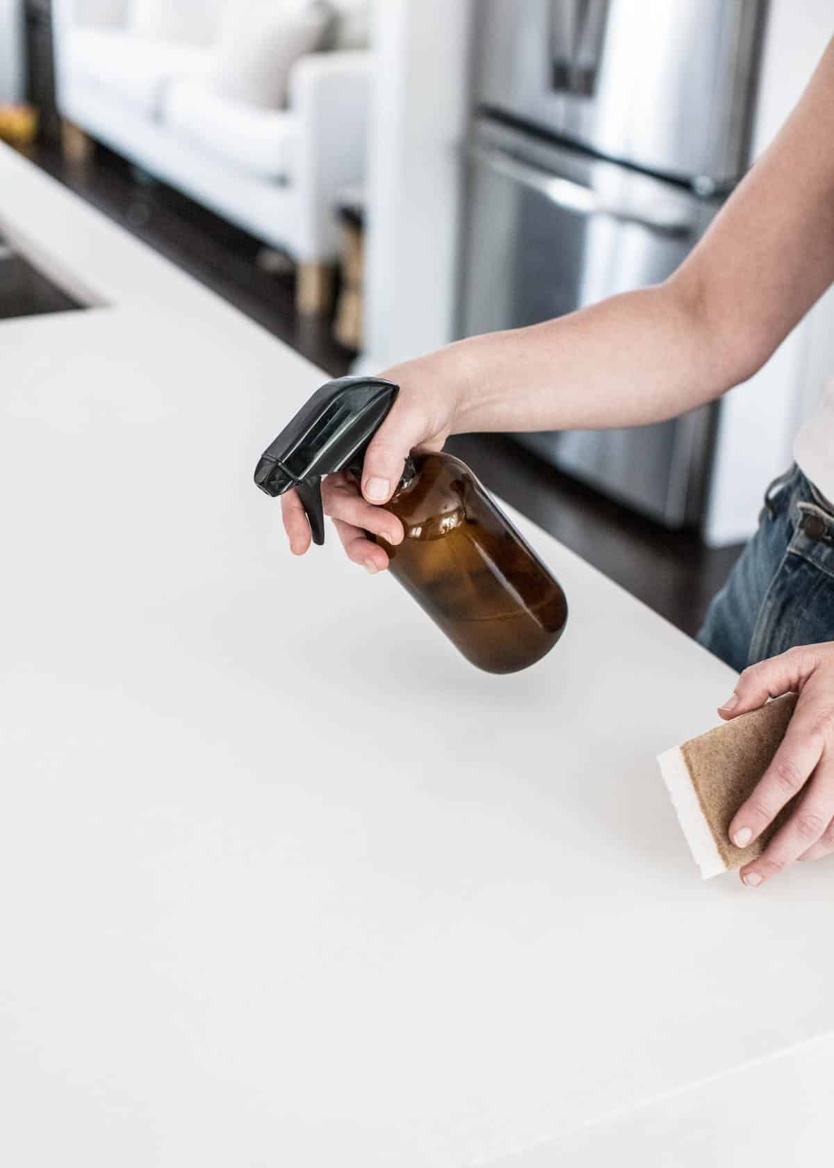 Woman cleaning the counter with an amber bottle.