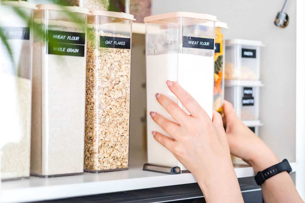 Woman's handing putting a container of flour back on a shelf in the cupboard.