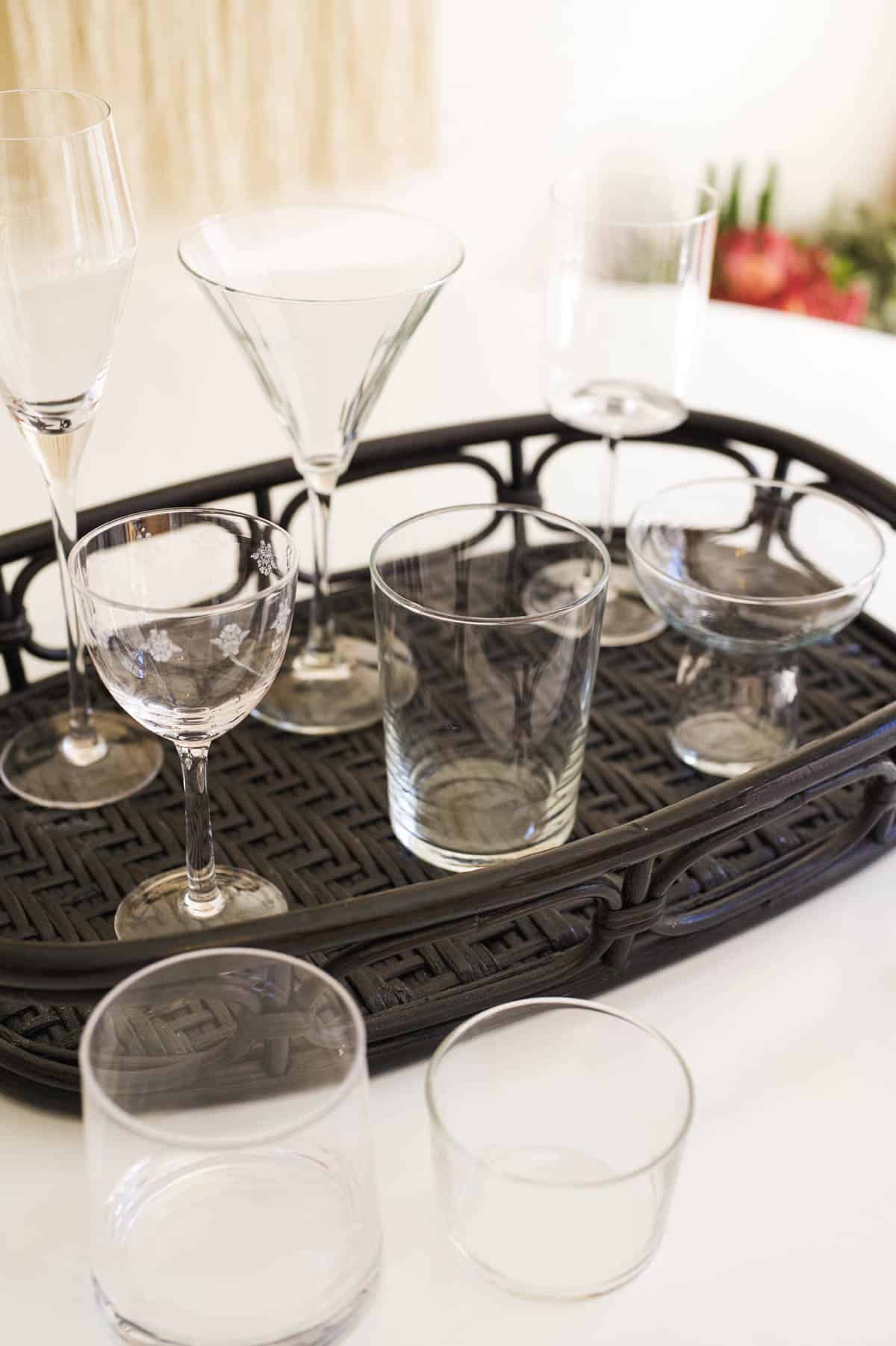 A variety of cocktail glassware on a table and on a black tray on a table.