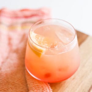 Grapefruit sunrise cocktail with vodka in a cocktail glass with piece of grapefruit as a garnish on a wood tray.