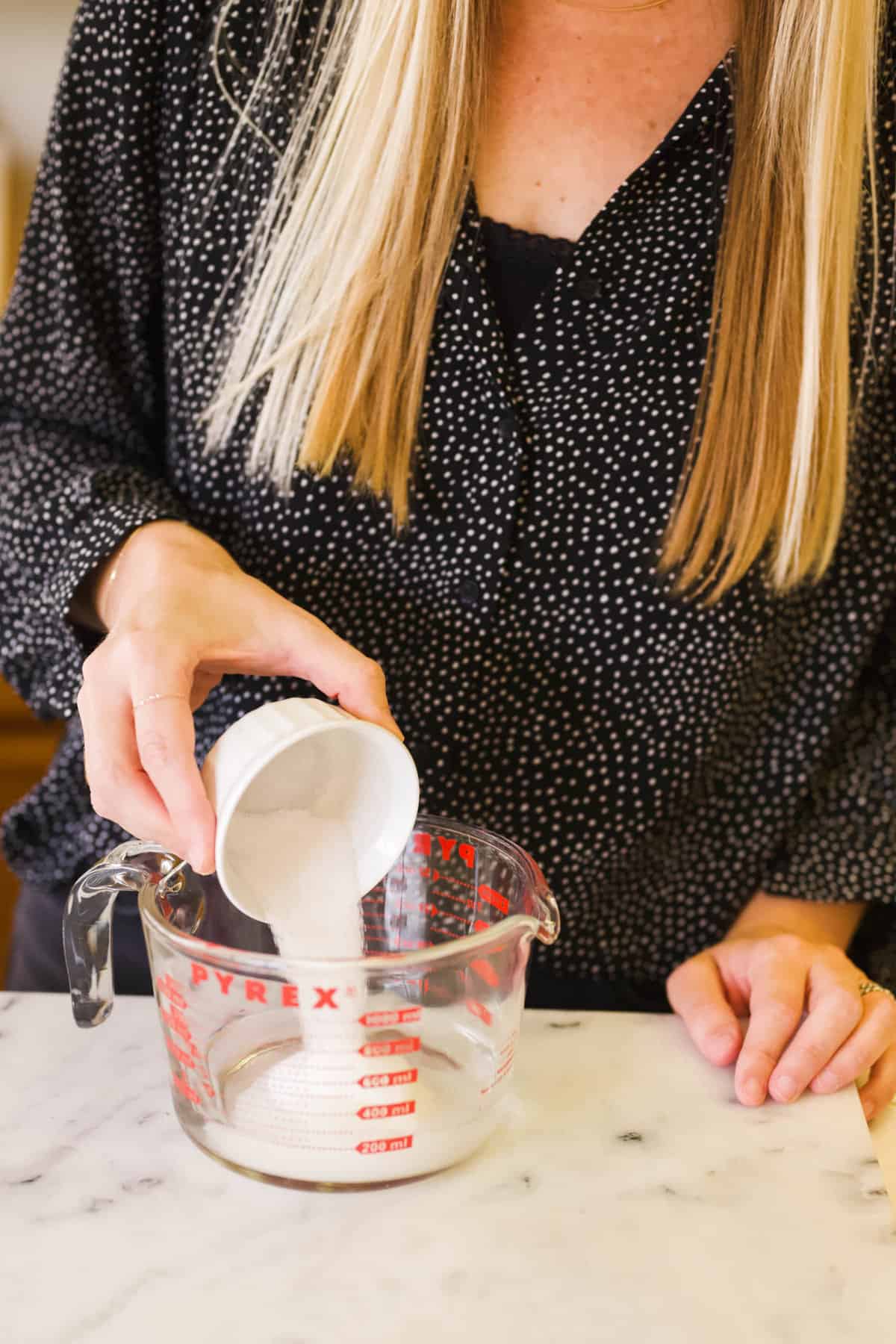 Woman adding sugar to water in a large glass measuring cup.