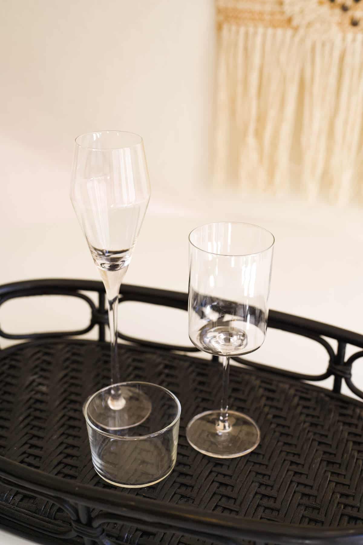 Two types of stemmed wine glasses and a short round glass on a black tray on a table.