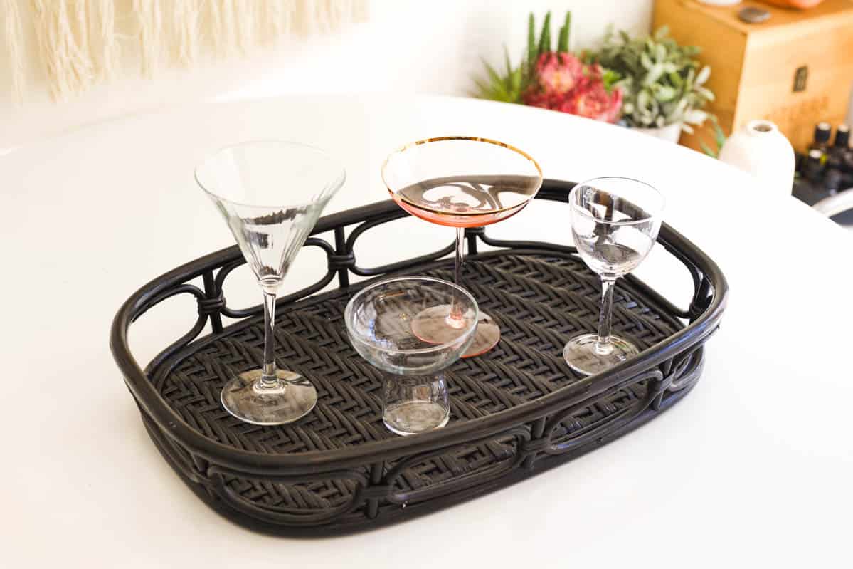 A coupe, martini, margarita and Nic and Nora glass on a black tray on a table.