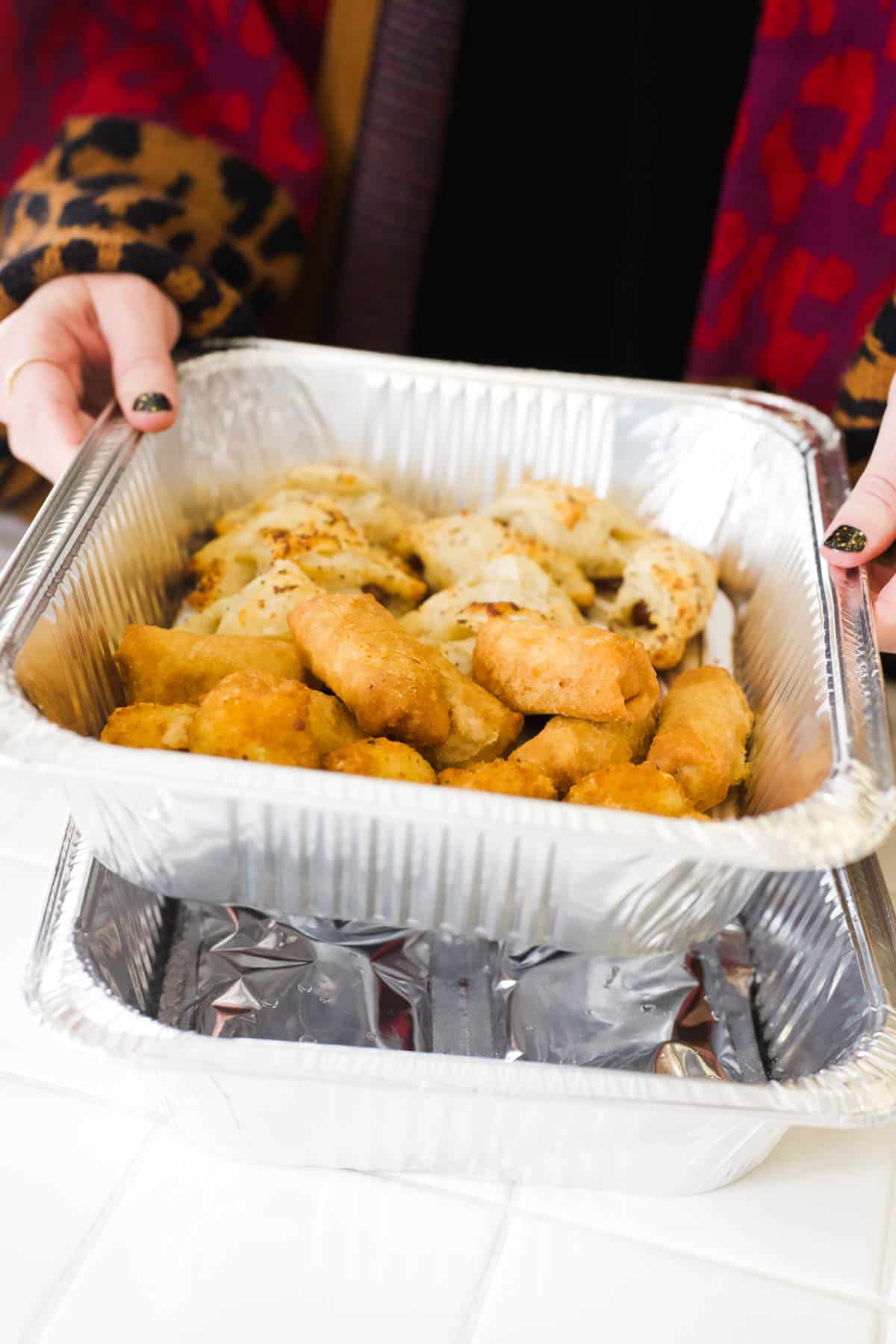 A woman placing a disposable tray of appetizers over another disposable tray with a heat pad.