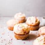 Six birthday cupcakes topped with vanilla buttercream frosting and sprinkles on a gray countertop.