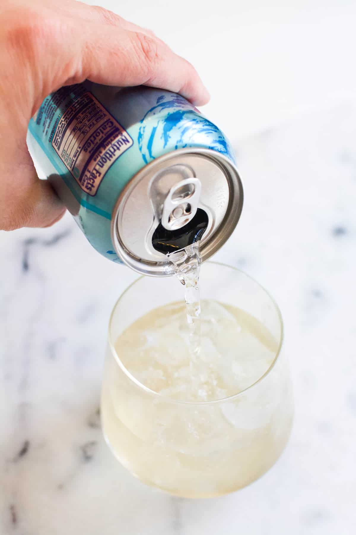 Pouring club soda into a glass with white wine and St. Germain.