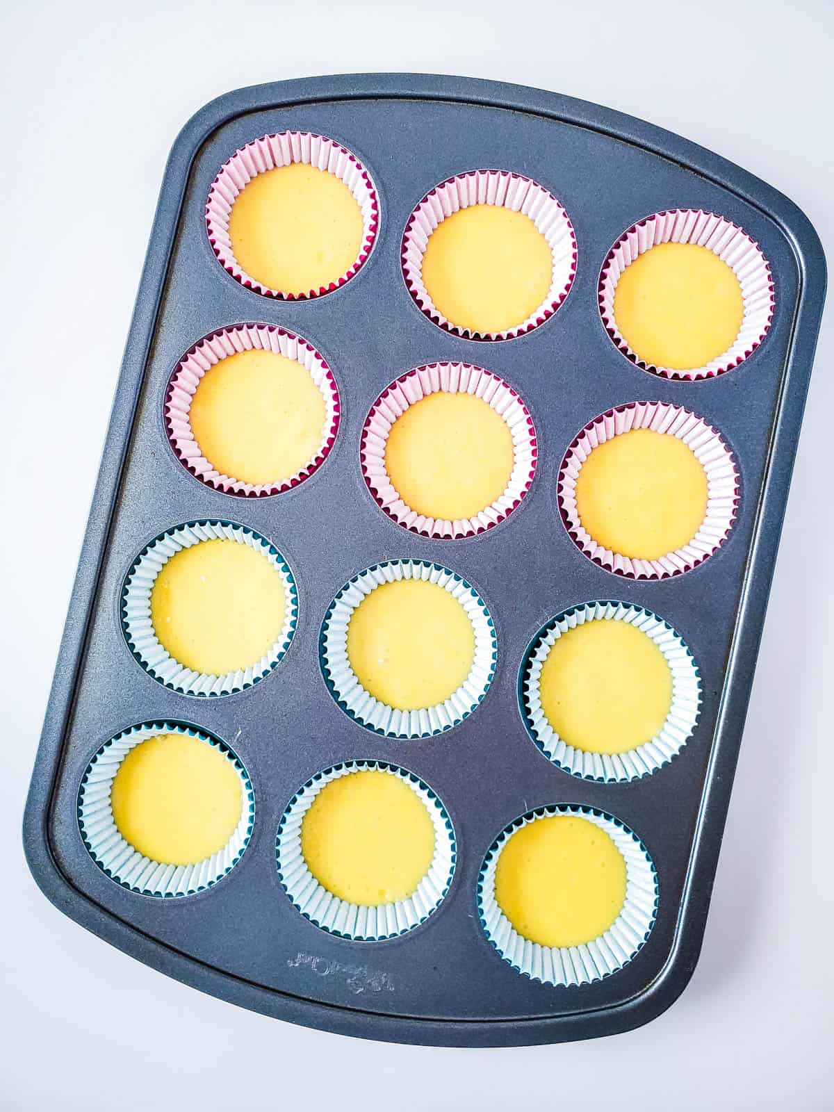 A cupcake tray with liners holding unbaked cupcake batter.