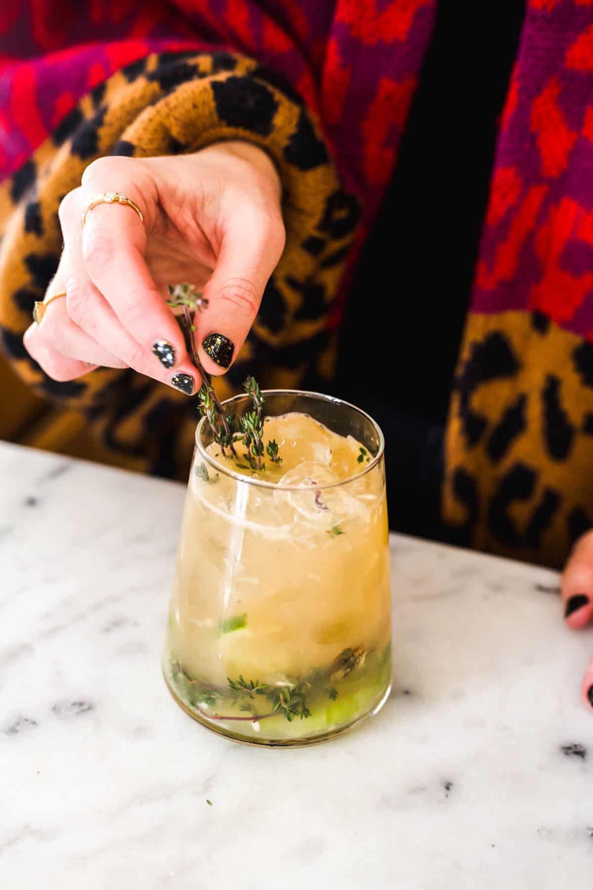 Woman garnishing a Grapefruit mocktail with fresh thyme.