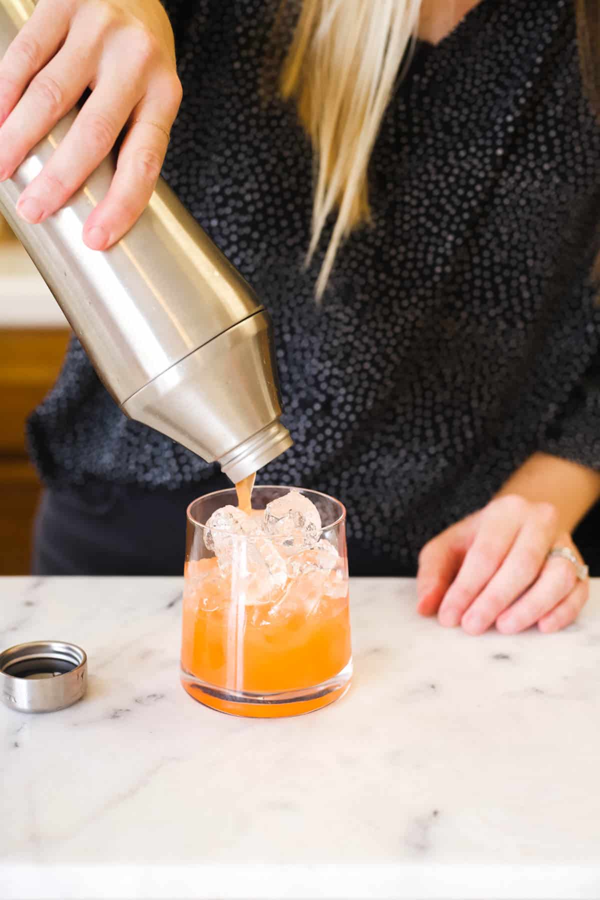 Straining a tropical spiced rum cocktail into a glass full of ice.