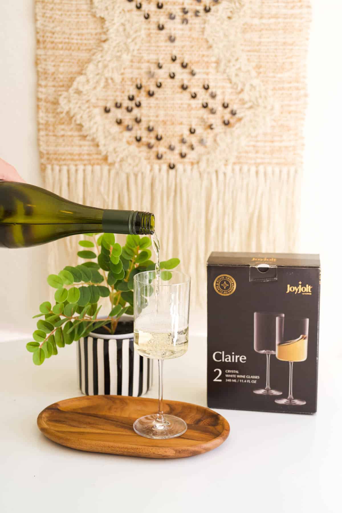 White wine glass on a table with wine being poured and the box next to it.