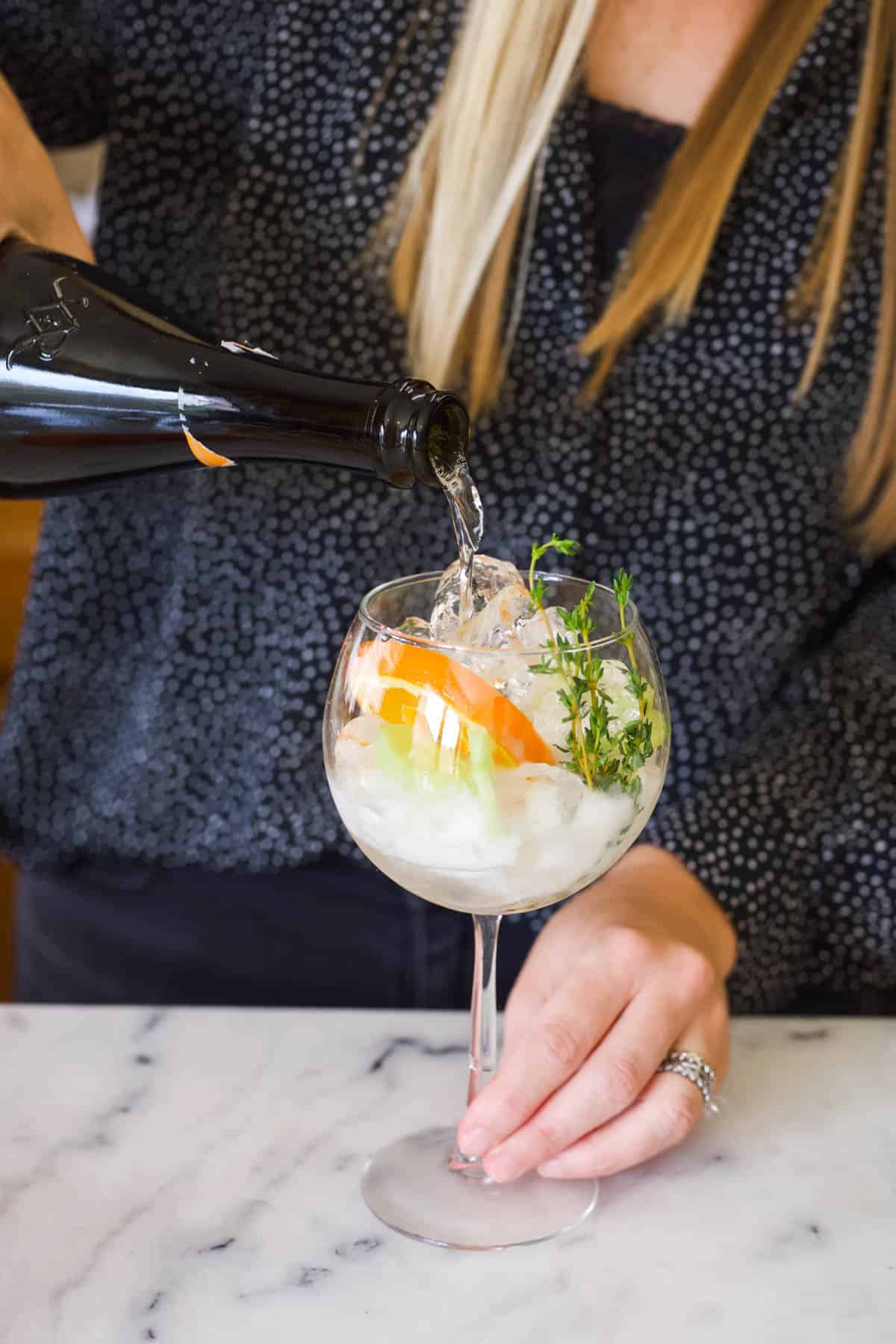 Woman adding prosecco to a Cointreau Spritz recipe.